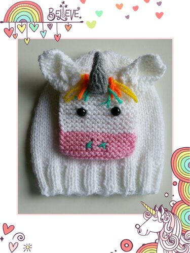 Weiß gestrickte Babymütze mit aufgesetztem Einhorn-Gesicht, Horn, Ohren und bunten Mähnenfäden