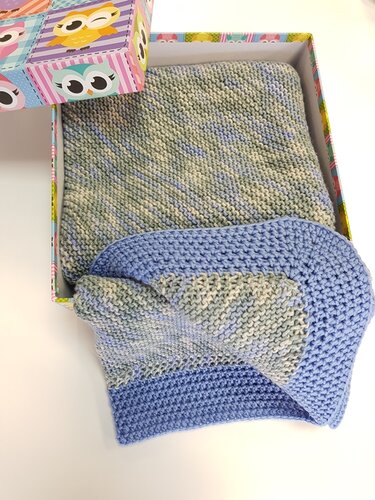 Gestrickte Babydecke in Blau- und Grüntönen, gefaltet in bunter Geschenkbox mit Eulenmotiv