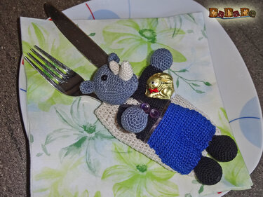 Gehäkelter Nashorn-Besteckhalter mit Besteck und kleinem Schokohasen auf floral gemusterter Serviette
