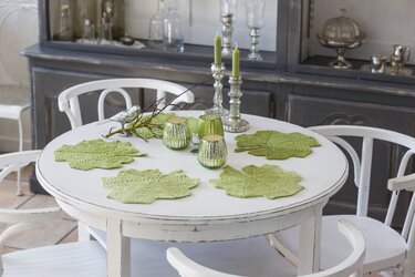 Weißer Tisch mit hellgrünen gestrickten Blatt-Deckchen, silbernen Kerzenhaltern und grünen Glaswindlichtern