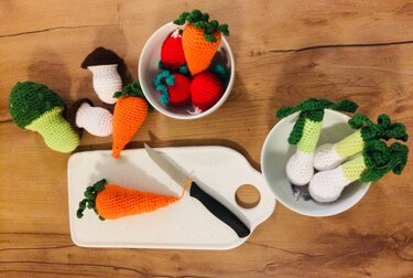 Gehäkelte Möhren, Pilze, Brokkoli und Lauch auf Schneidebrett und in Schälchen