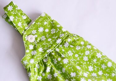 Nahaufnahme eines grünen Stoffes mit weißem Blumenmuster, Träger und weißem Knopf.