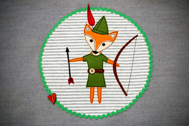 Runde Applikation: Fuchs mit grüner Tunika, Zipfelhut, Bogen und Pfeil auf gestreiftem Stoffkreis mit grüner Zackenborte und rotem Herzknopf