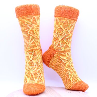 Paar orangener, gestrickter Socken mit gelbem Sonnenmuster auf hellem Hintergrund