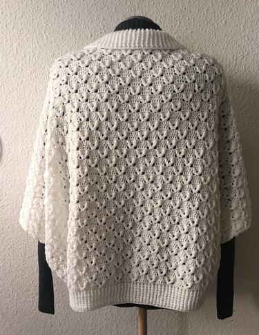 Rückansicht eines weißen gehäkelten Seelenwärmers auf einem Mannequin mit Lochmuster und Rippenbündchen