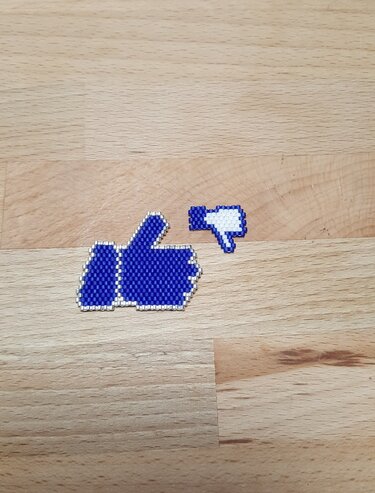 Zwei pixelige Perlen-Icons auf Holz: großer blauer Daumen hoch und kleiner Daumen runter.