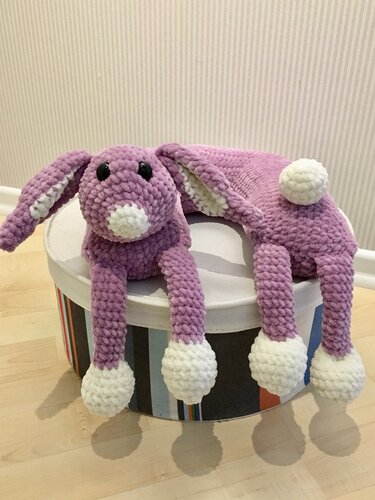 Gehäkeltes violettes Hasenkissen mit langen Beinen, weißen Pfoten und Bommel