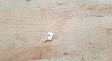 Kleine, detailreiche Mausfigur aus weißen Perlen mit rosa Ohren auf hellem Holzgrund.