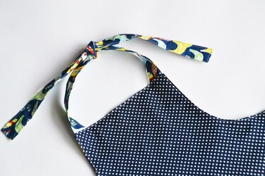 Nahaufnahme: dunkelblauer Stoff mit weißen Pünktchen und buntem Bindeband mit Tiermotiven, geknotet.