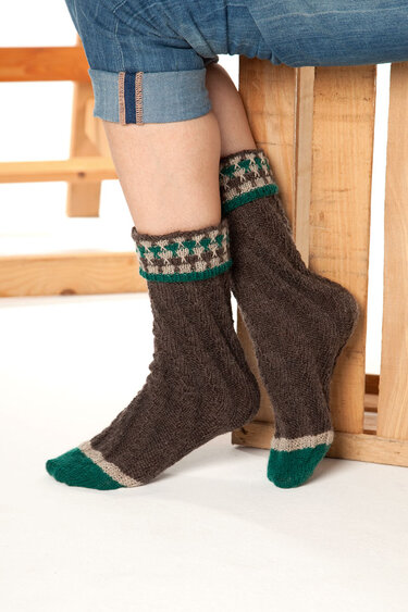 Dunkelbraune gestrickte Socken mit grün-cremefarbenem Rautenmuster am Umschlagbündchen und grünen Zehen, getragen zu Jeans.