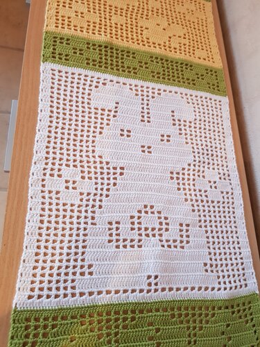 Filethäkel-Tischläufer mit durchbrochenem Hasenmotiv und gelb-grünen Randstreifen auf Holztisch
