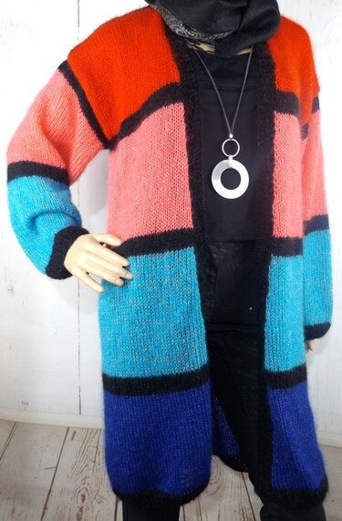 Mannequin trägt offenen, lang gestrickten Damencardigan mit orange-, rosa-, türkis- und blaufarbenen Feldern und schwarzen Linien
