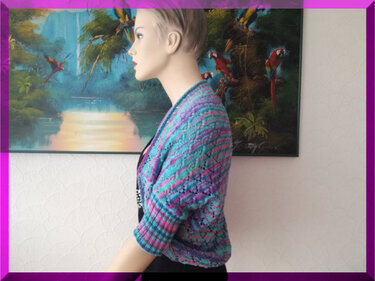 Schaufensterpuppe mit kurzärmeligem, offen geschnittenem Seelenwärmer aus Strick in Türkis, Pink und Lila.