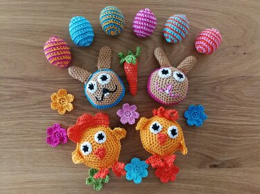 Bunte gehäkelte Osterfiguren mit Hasenköpfen, Küken, gestreiften Eiern, Möhre und Blumen auf Holz