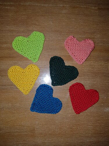 Sechs farbige gehäkelte Herzen auf Holztisch dekorativ arrangiert