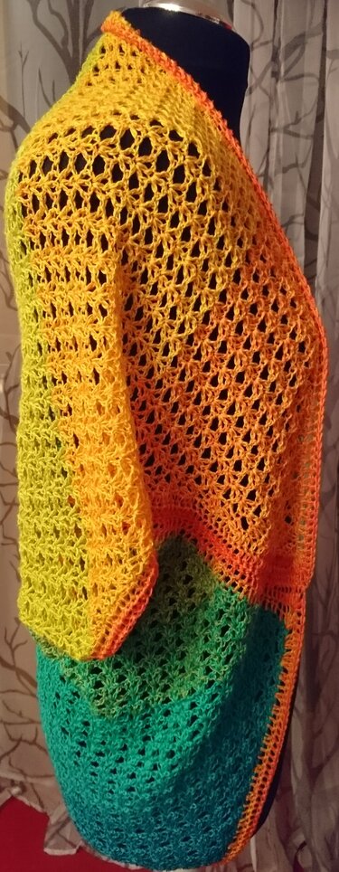 Gehäkelter Damen-Seelenwärmer in Gelb, Orange und Türkis mit durchbrochenem Muster auf einer Schneiderpuppe.