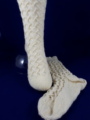 Cremefarbene gestrickte Kniestrümpfe mit Ajour- und Zopfmuster auf dunklem Hintergrund