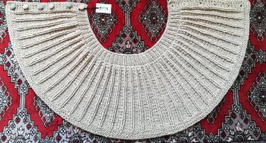 Beige gestrickte Rundpasse mit schmalen vertikalen Rippen und Knöpfen an der Kante