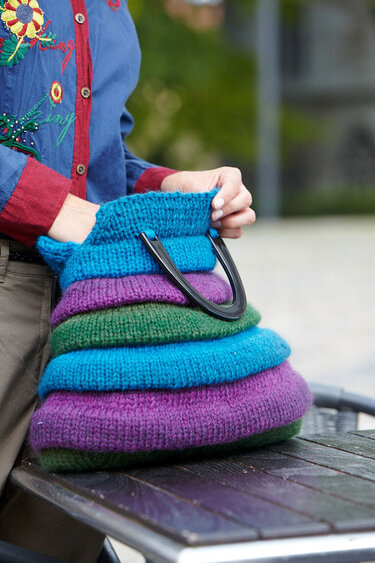 Hand hält mehrfarbige, gestrickte Damentasche mit gestuften Lagen und schwarzen Griffen