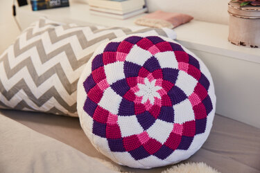 Rundes Mandala-Häkelkissen in Pink, Violett und Weiß neben einem Zickzack-Kissen