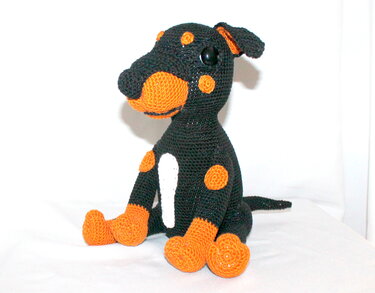 Gehäkelter sitzender Amigurumi‑Hund in Schwarz mit orangefarbenen Details und weißer Brust