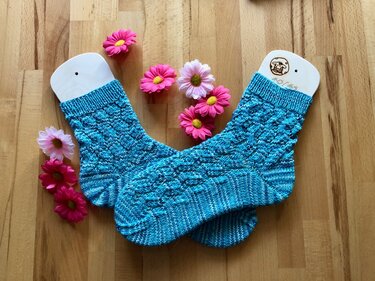 Türkis melierte gestrickte Damensocken mit Ajourmuster auf Holzsockenspannern und rosa Blumen