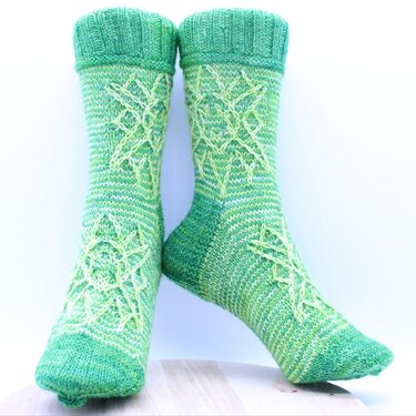 Pair of green knitted crew socks with raised star cable motifs and ribbed cuffs