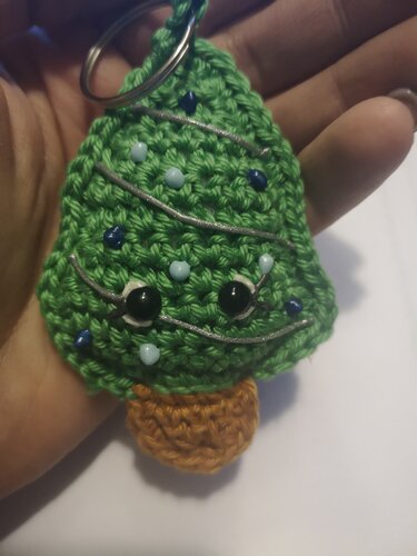 Gehäkelter grüner Weihnachtsbaum-Schlüsselanhänger mit farbigen Perlen, aufgestickten Augen und silbernen Girlanden in einer Hand