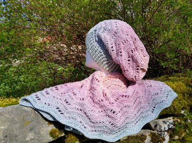 Mannequin mit gehäkelter Slouch-Mütze und passendem Dreieckstuch in Rosa-Grau Farbverlauf auf Steinmauer