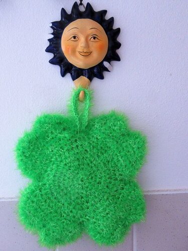 Grünes, flauschiges vierblättriges Kleeblatt aus Garn hängt vor einem Sonnenmotiv