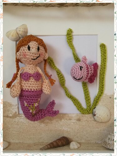 Gehäkelte Meerjungfrau mit Zöpfen und lila-rosa Schwanz, kleiner Amigurumi-Fisch, gehäkeltes Seegras und Muscheln