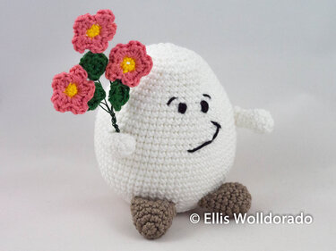 Lächelndes weißes Amigurumi
Ei hält einen Strauß rosa Häkelblumen