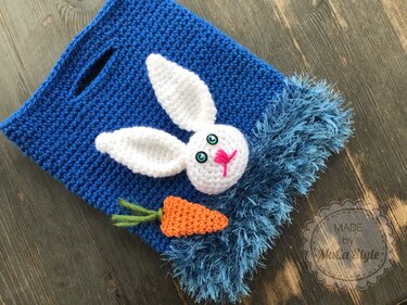 Blaue gehäkelte Tasche mit weißem Hasenkopf, türkisfarbenen Augen, pinker Nase und gehäkelter Karotte