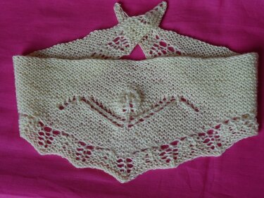 Cremefarbenes gestricktes Baby-Dreieckstuch mit Lochkante und Bändchen auf pinkem Hintergrund