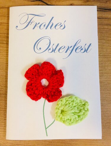 Schlichte Osterkarte mit 'Frohes Osterfest' Schrift und schnell gehäkelter roter Blüte samt grünem Blatt