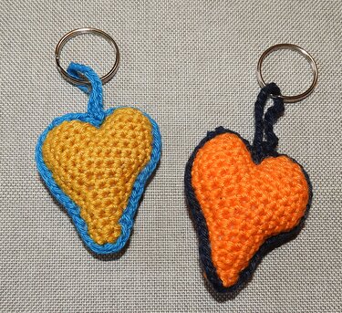 Zwei gehäkelte Herz-Schlüsselanhänger, gelb-blau und orange-dunkelblau, auf grauem Stoff