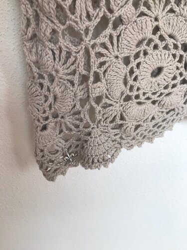 Detailaufnahme einer beigen Häkelspitze mit runden Motiven und Lilienanhänger