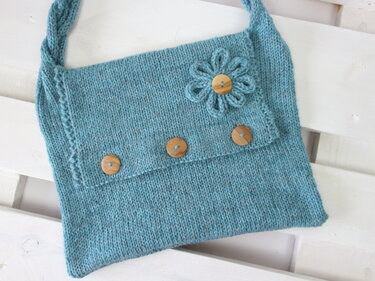 Teal hand-knitted shoulder bag with fold-over flap, three wooden buttons and a yarn flower appliqué