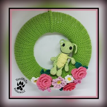 Grüner gehäkelter Türkranz mit kleinem Amigurumi-Frosch und rosa sowie weißen Häkelblumen
