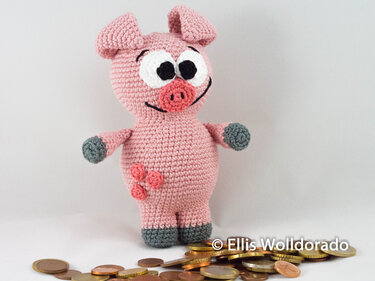 Rosa gehäkeltes Sparschwein-Amigurumi mit großen Augen, grauen Pfoten und drei Röschen am Bauch, stehend auf Münzen vor hellem Hintergrund.