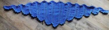 Blaues gestricktes Dreieckstuch mit gewelltem Rand auf Holzboden