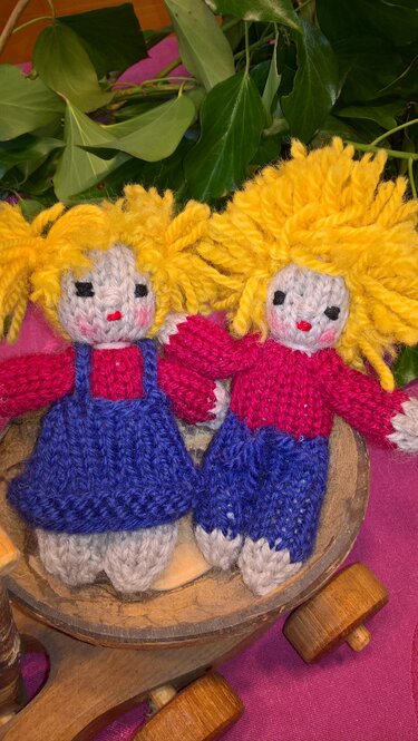 Zwei gestrickte Amigurumi-Puppen mit gelbem Haar in einer Holzschale