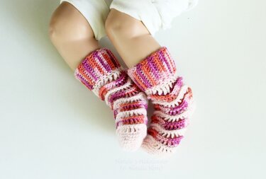 Infant legs wearing pink, purple and orange crocheted ruffle socks with ribbed cuffs