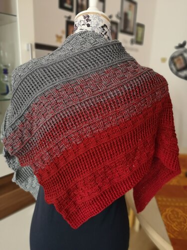 Gehäkeltes Dreieckstuch mit Farbverlauf von Grau zu Rot und strukturiertem Muster, auf einer Schneiderpuppe drapiert.