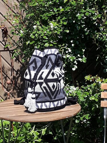 Gehäkelter Rucksack mit schwarz-weiß-grauem geometrischem Muster und weißen Quasten auf Holztisch