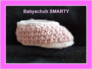 Gehäkelter Babyschuh in Rosa und Weiß auf dunklem Hintergrund