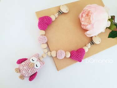 Rosa gehäkelte Schnullerkette mit Eulenanhänger, Herzen und Holzperlen auf hellem Hintergrund.