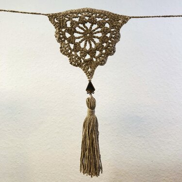 Handgehäkelter Wandbehang in Naturtönen mit Mandala-Muster und langer Quaste.