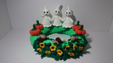 Gehäkelter Kranz mit drei weißen Geistern, orangefarbenen Kürbissen und gelben Blumen
