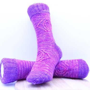 Nahaufnahme einer lila-pinken gestrickten Socke mit geripptem Bündchen und Rautenmuster